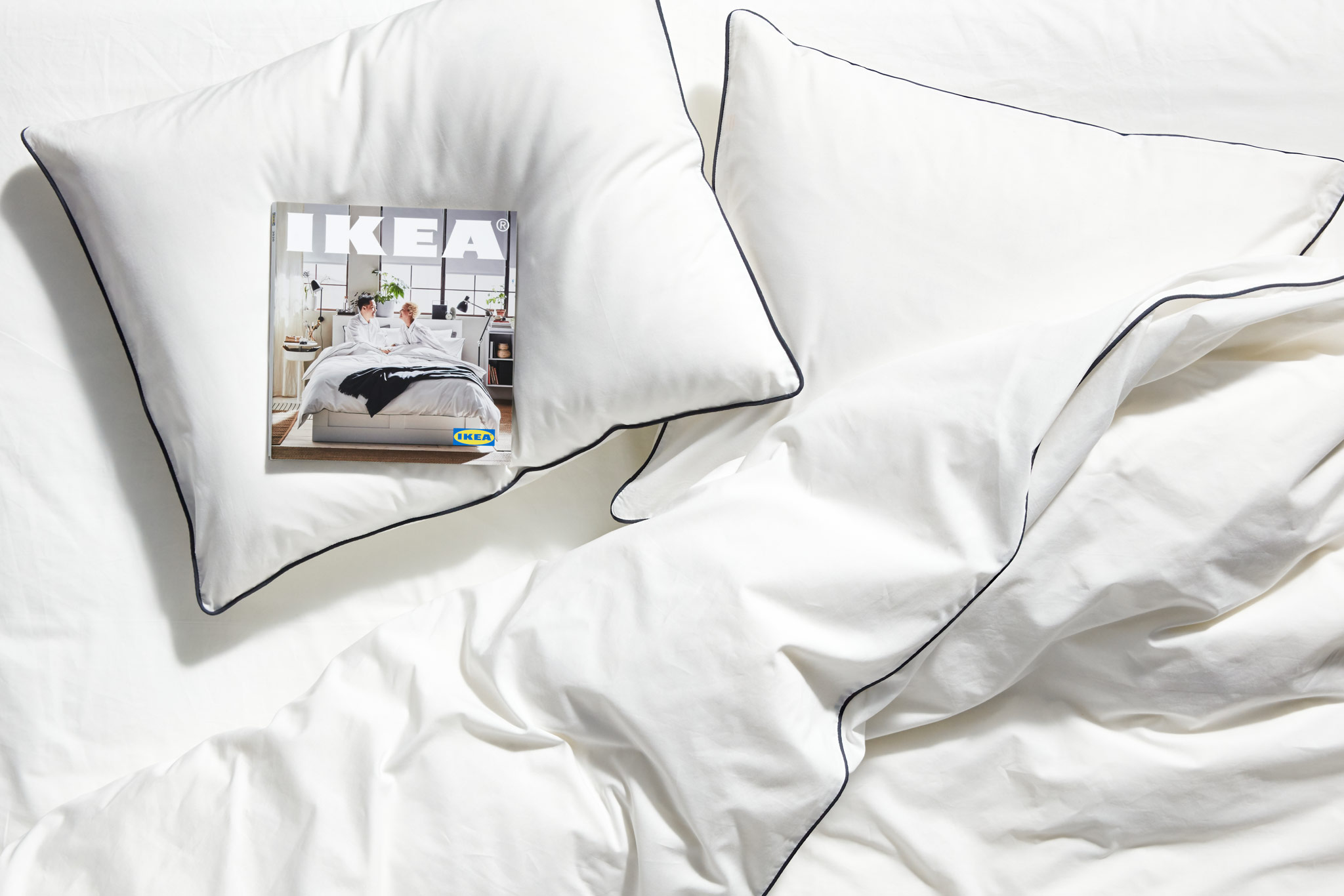 White pillows on a bed with white bed covers, and a copy of the 2020 IKEA Catalogue laying on one of the pillows.