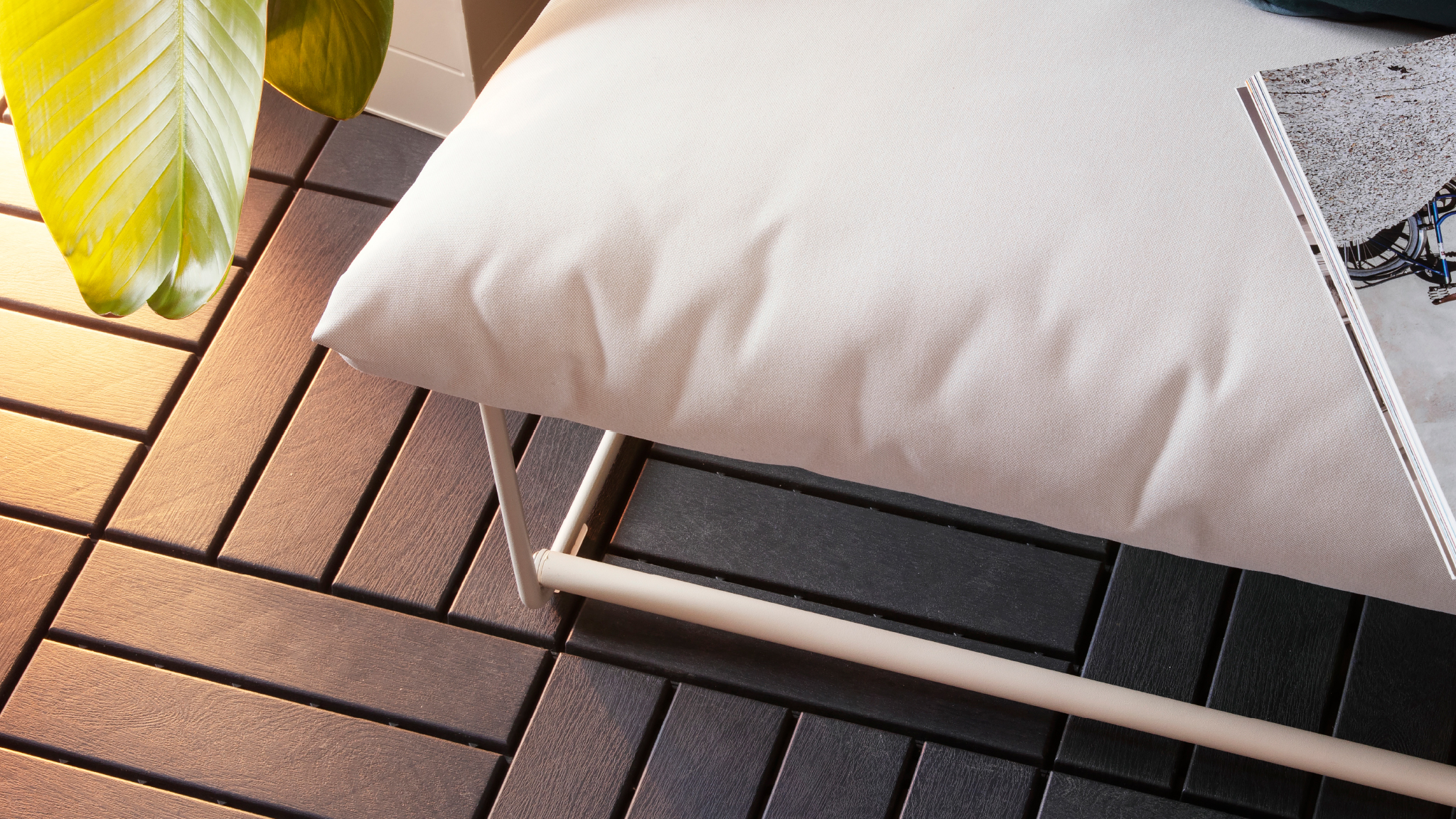 Wooden-look outdoor flooring in sections, under an outdoor sofa with white upholstery and a book on it.