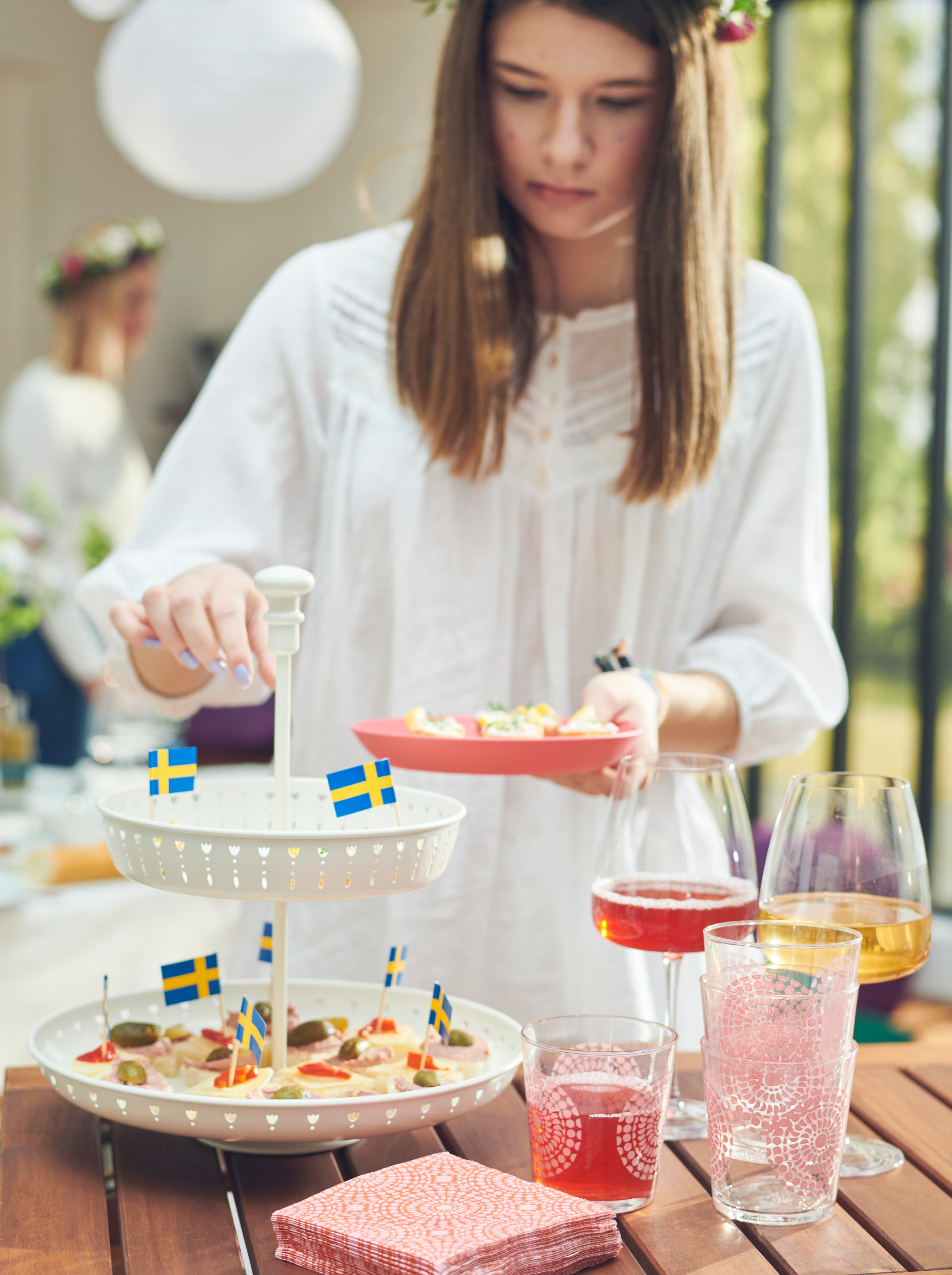 Young woman serving herself bites from a GARNERA serving stand, filled DYRGRIP glasses placed on the table next to it.